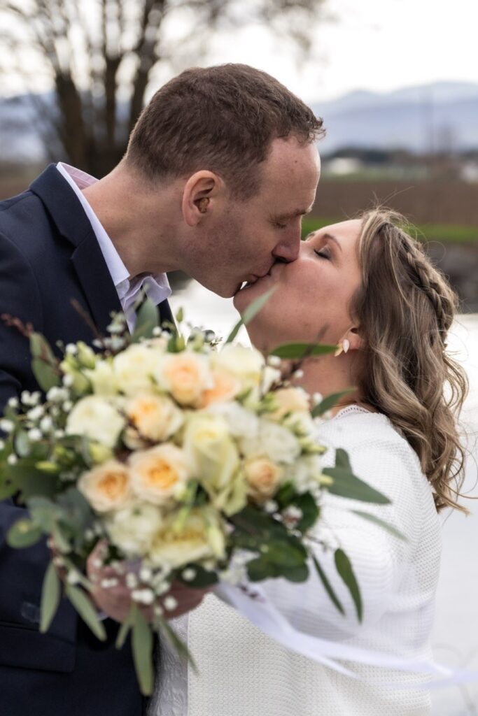 Photographie d'un couple marié qui s'embrassent à l'extérieur avec le bouquet